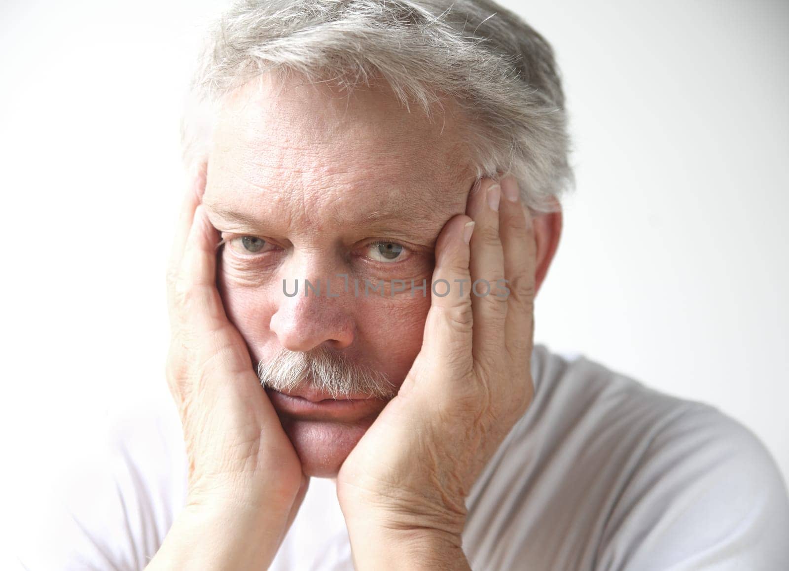 senior man rests his face in his hands and looks disappointed or bored