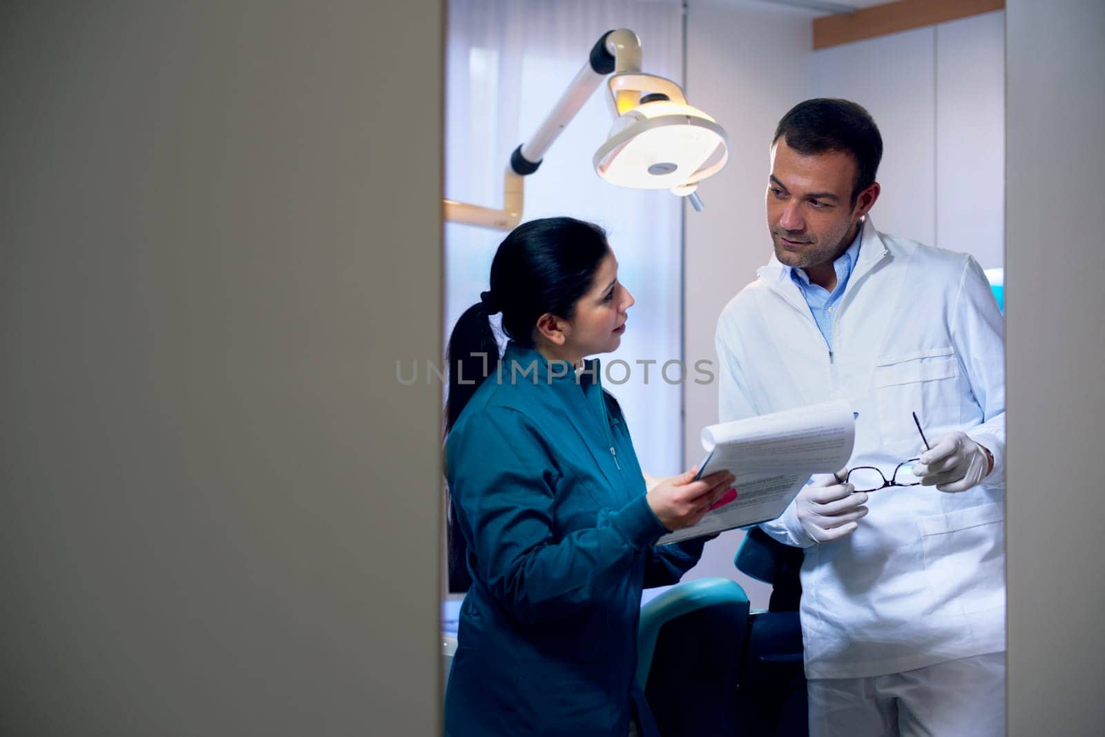 Dentist talking with female assistant in studio and looking at files. Copy space