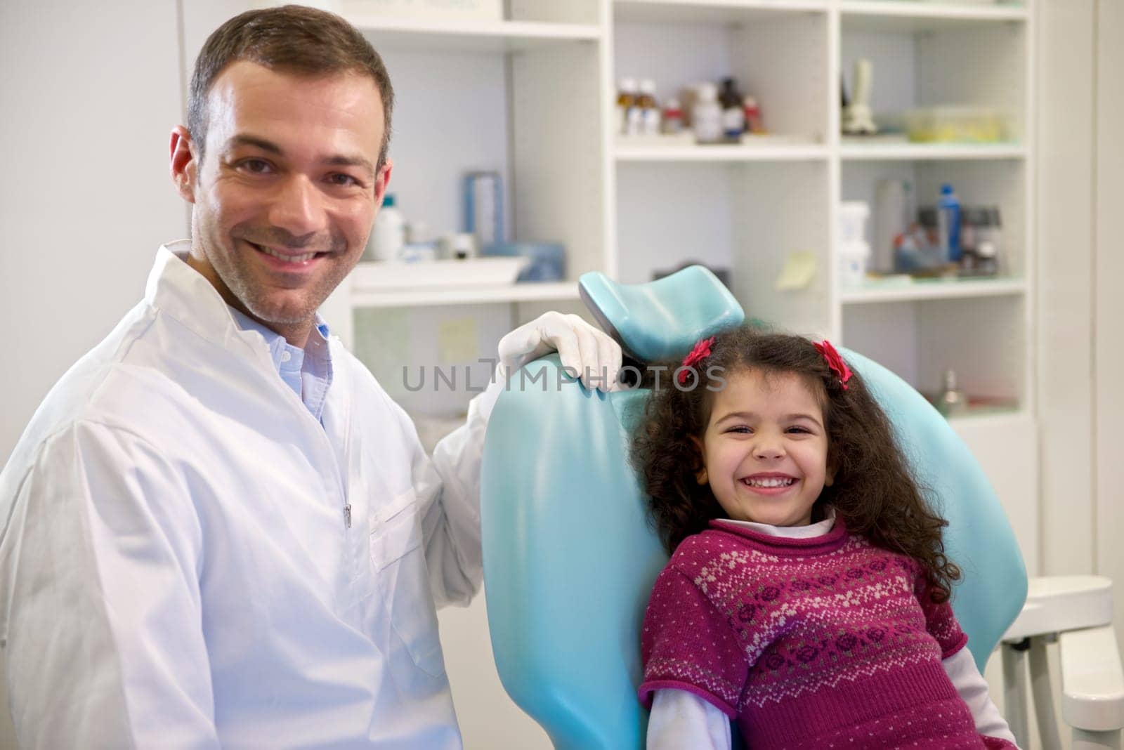 Doctor during visit of female child in dental clinic, portrait of young baby girl looking at camera and smiling