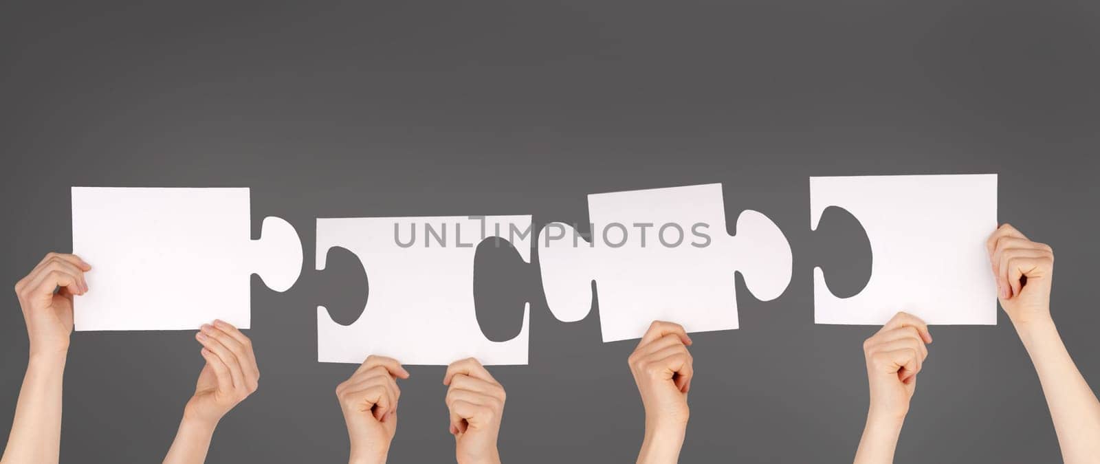 hands holding four pieces of a puzzle with copy space, gray background