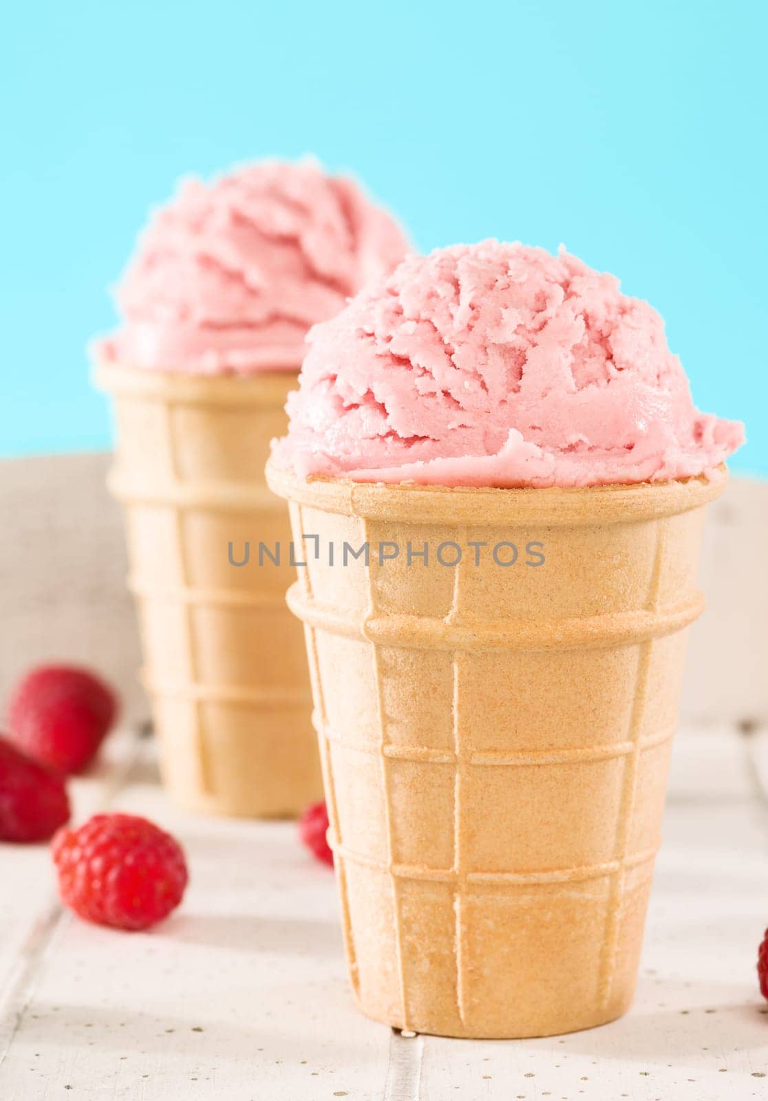 Raspberries ice cream in front of other in waffle on white wood