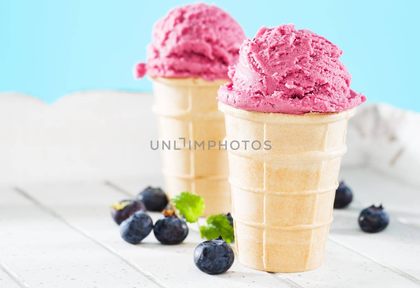 Two waffles with ice cream and blueberries on white wood
