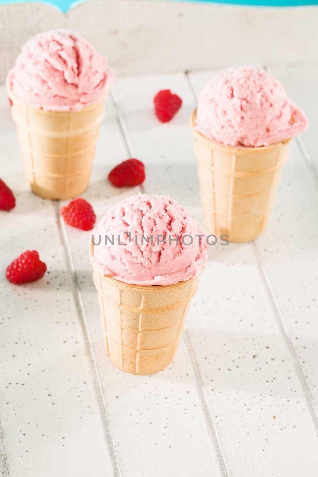 Three waffles with ice cream and raspberries on white wood
