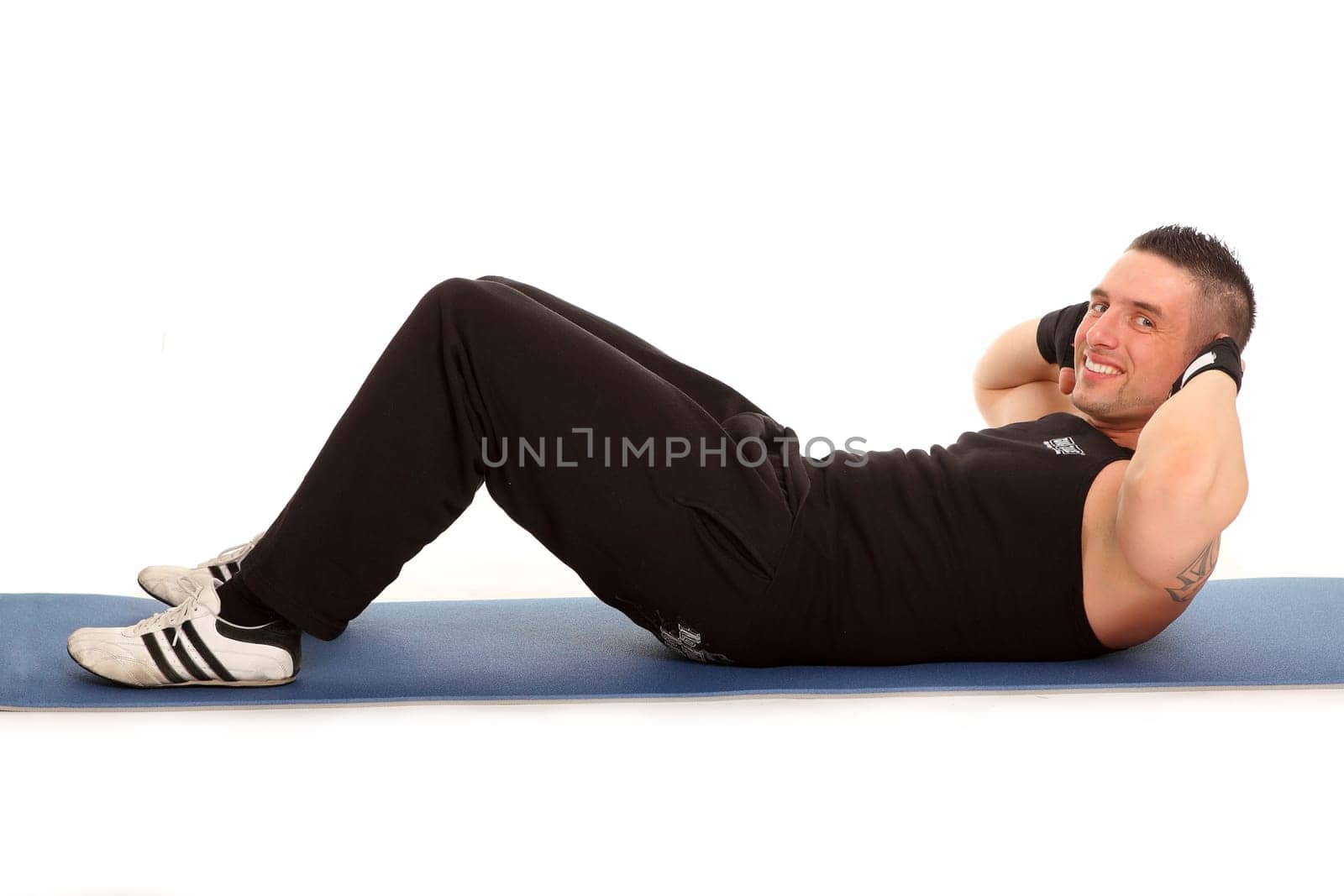 A young man is about to do a sit-up and looks friendly into the camera