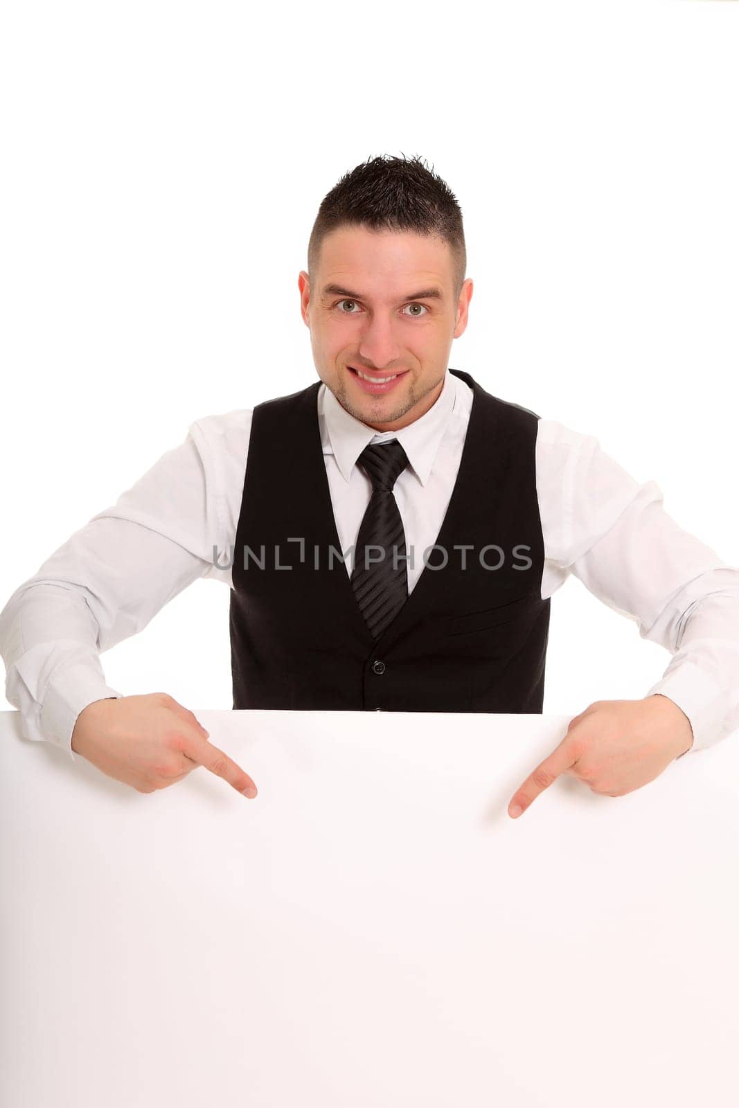 Photo of a businessman pointing at a white sign with both fingers while looking kindly at the camera