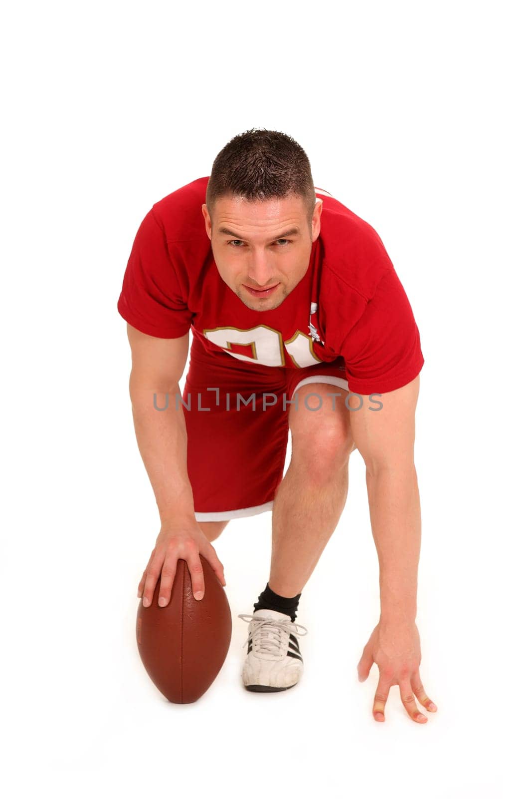 The photo shows a young man standing a football on the ground at the bottom and looking forward