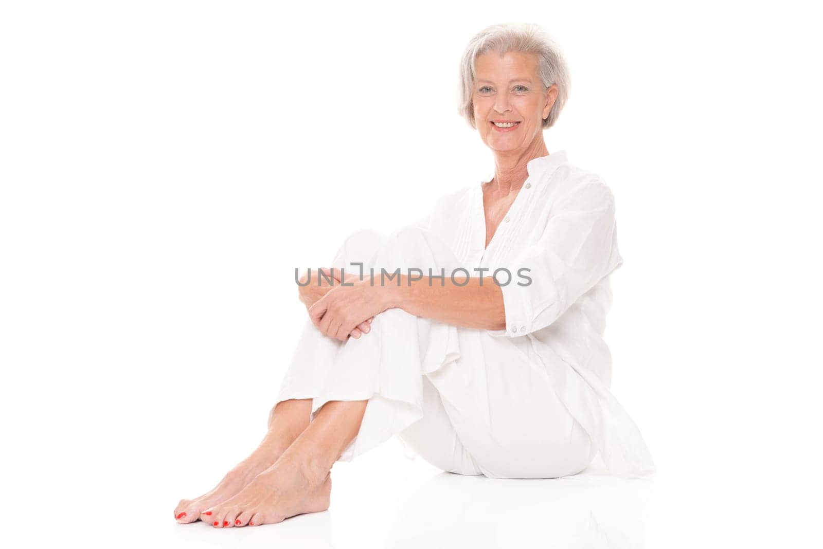 Active senior woman sitting on floor against white background