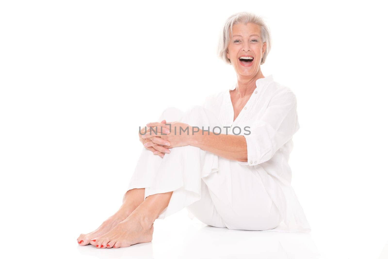 Active senior woman sitting on floor against white background