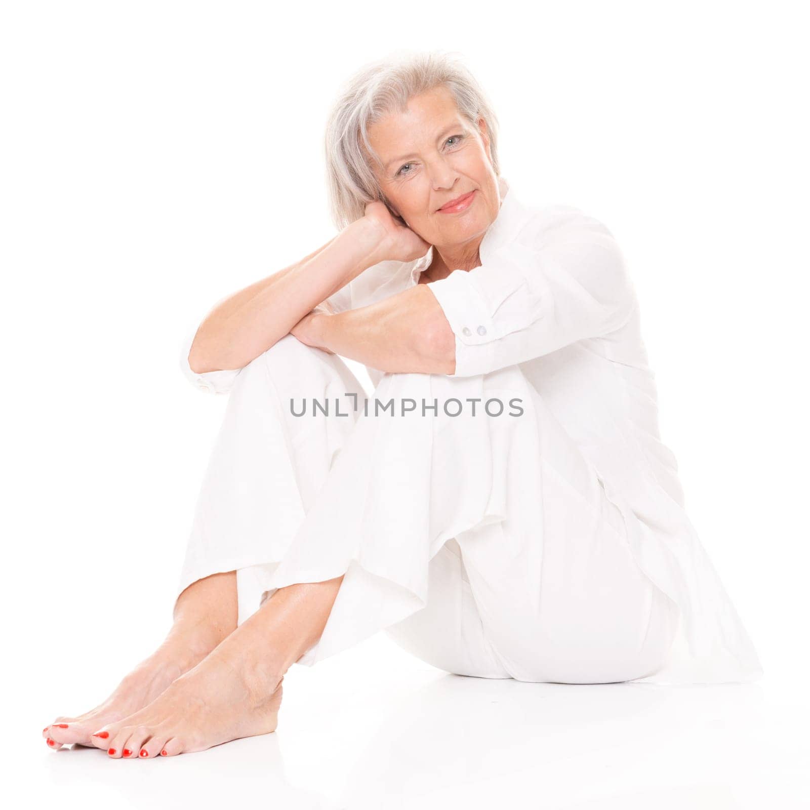 Active senior woman sitting on floor against white background
