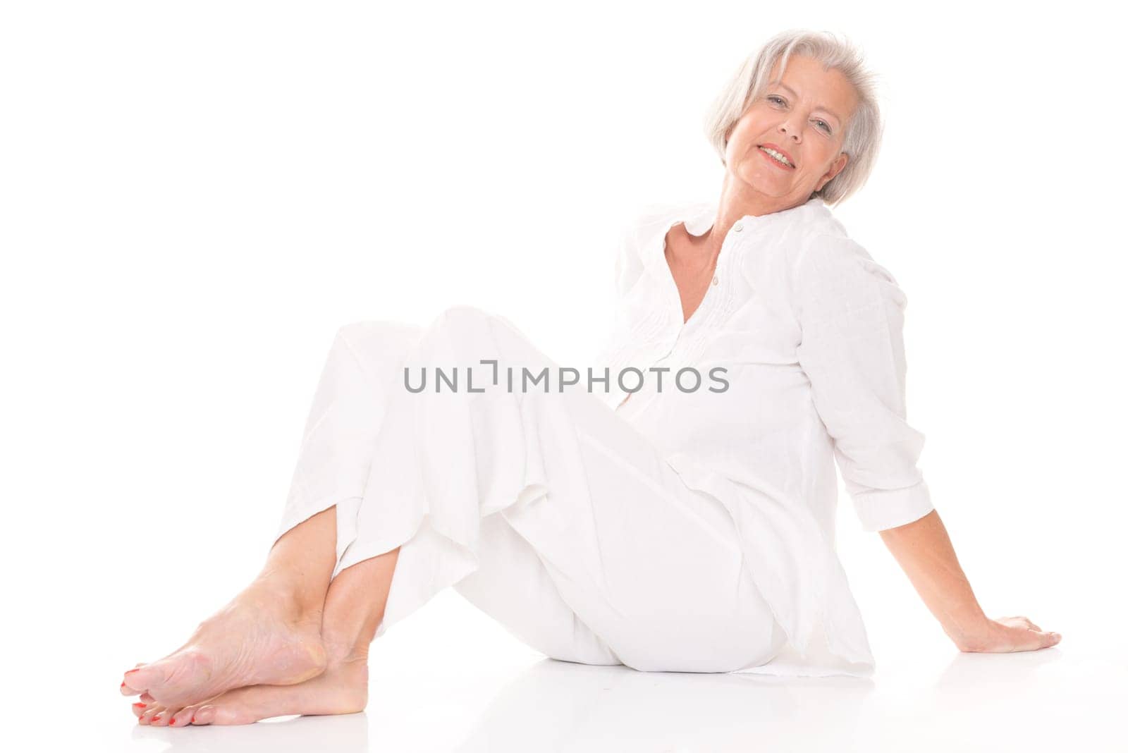Active senior woman sitting on floor against white background