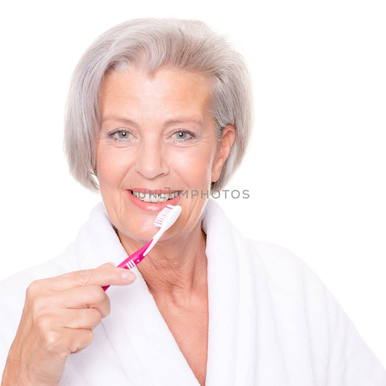 Studio shot of an elderly woman in a white bathrobe and using a toothbrush