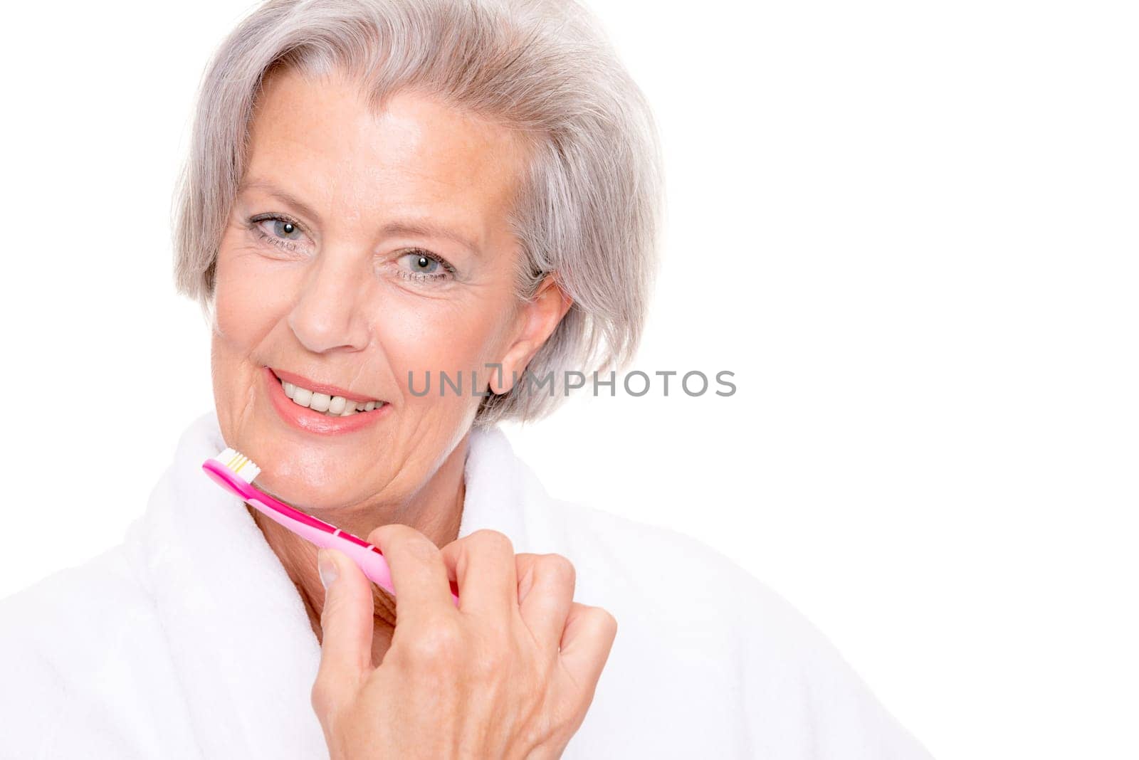 Studio shot of an elderly woman in a white bathrobe and using a toothbrush