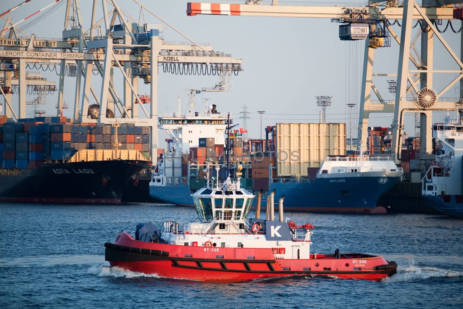 Tugboat crossing the busy Elbe River in Hamburg Harbor, Germany, with freighters in background.