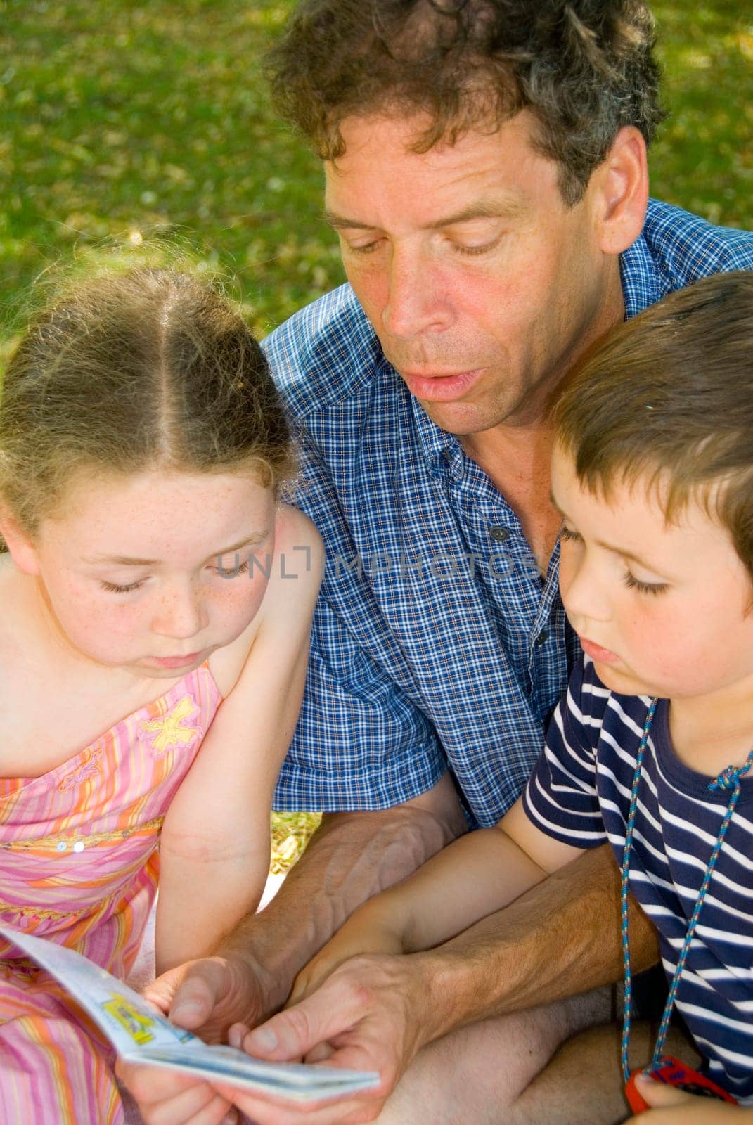 father with daughter and son reading in park