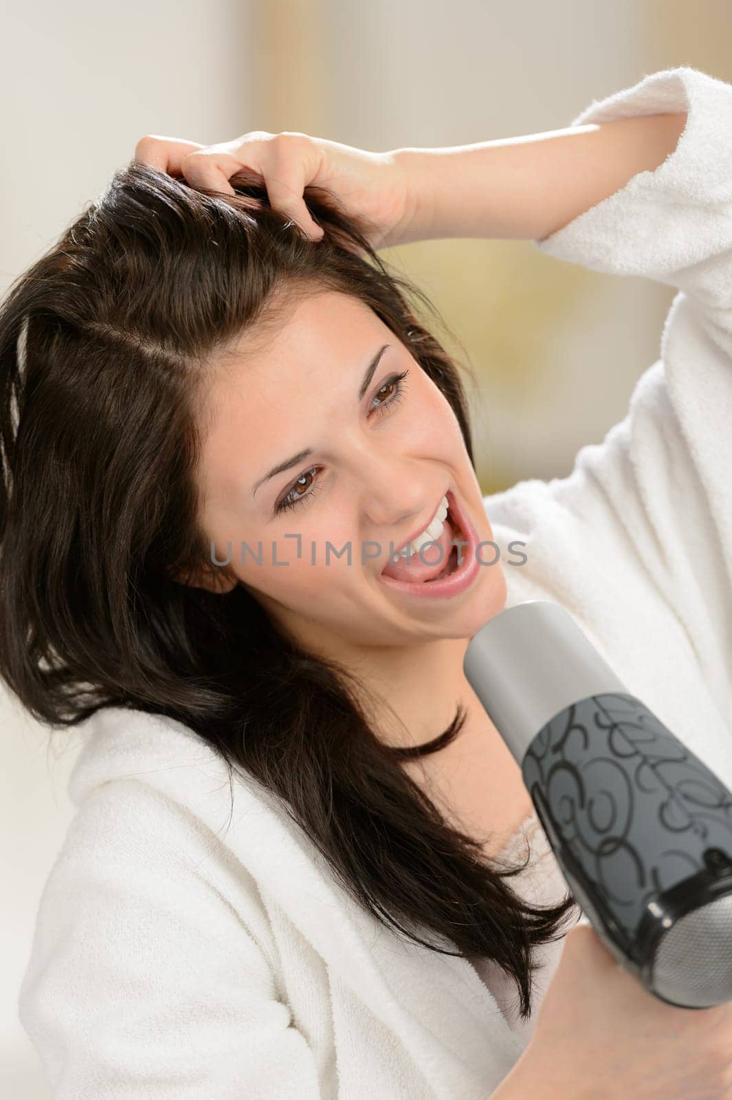 Joyful girl singing with blow dryer in bathrobe