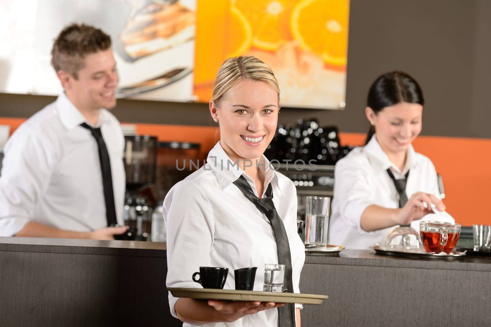 Confident waitress serving coffee with tray colleagues working behind