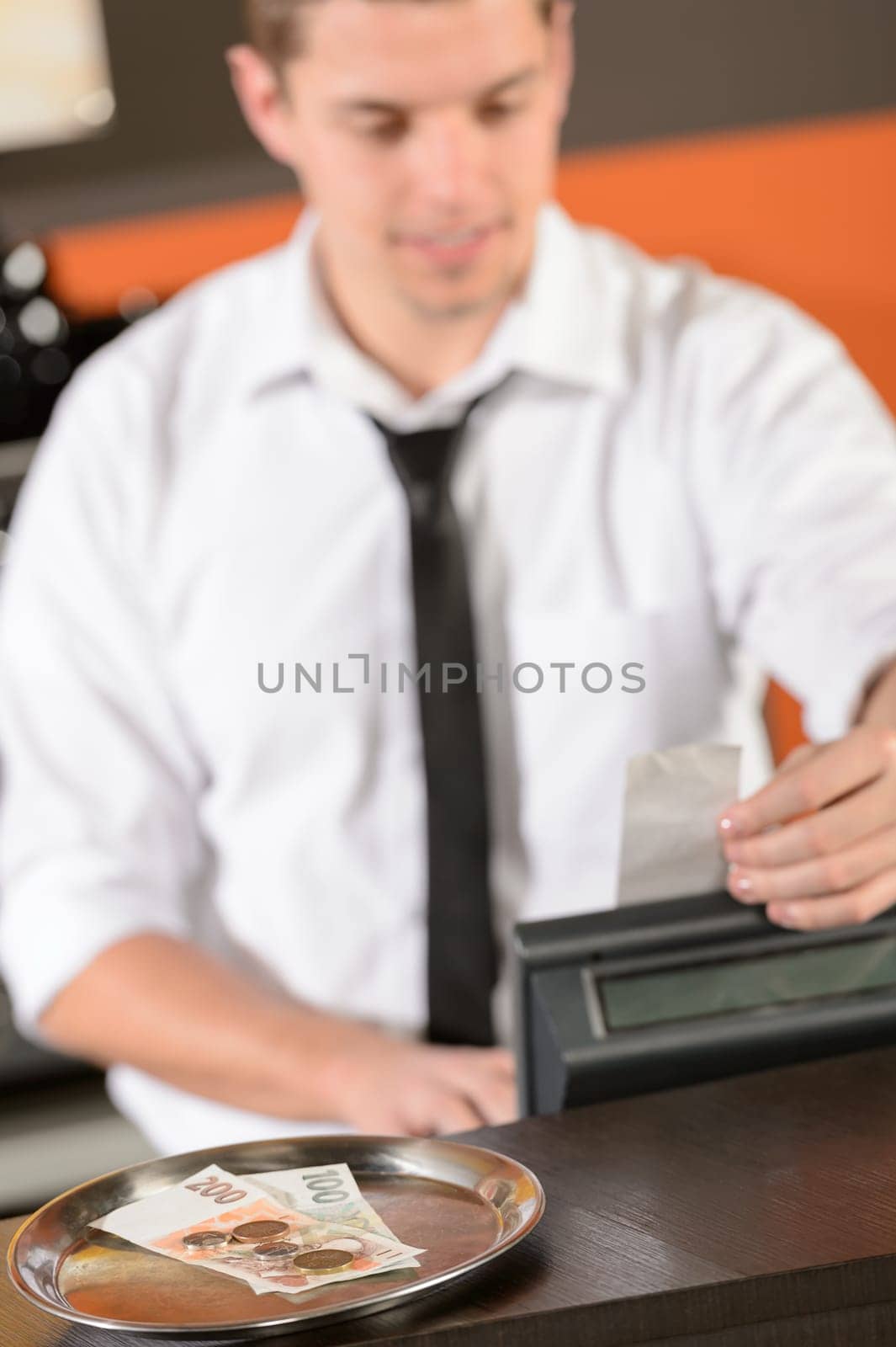 Young bartender in uniform taking cash czech crowns in bar