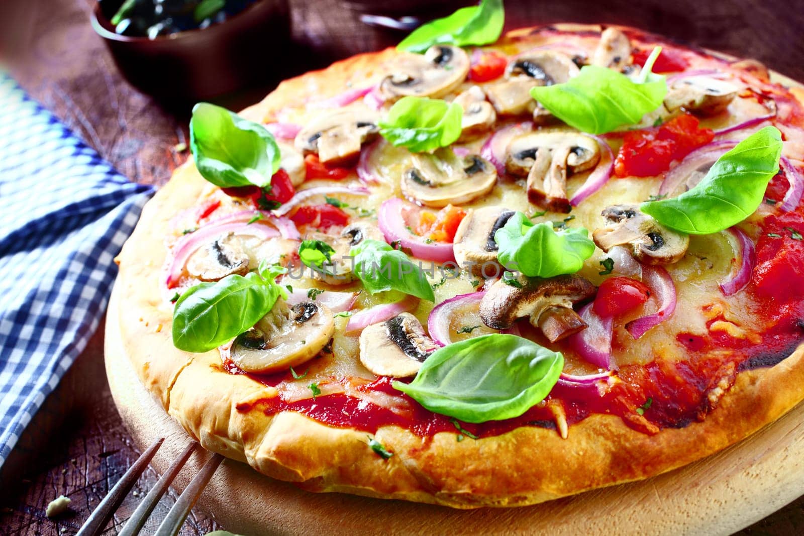 Delicious vegetarian pizza topped with tomato, melted cheese, mushrooms, onions and fresh basil leaves served on a wooden board, high angle view. More pizza at my port.