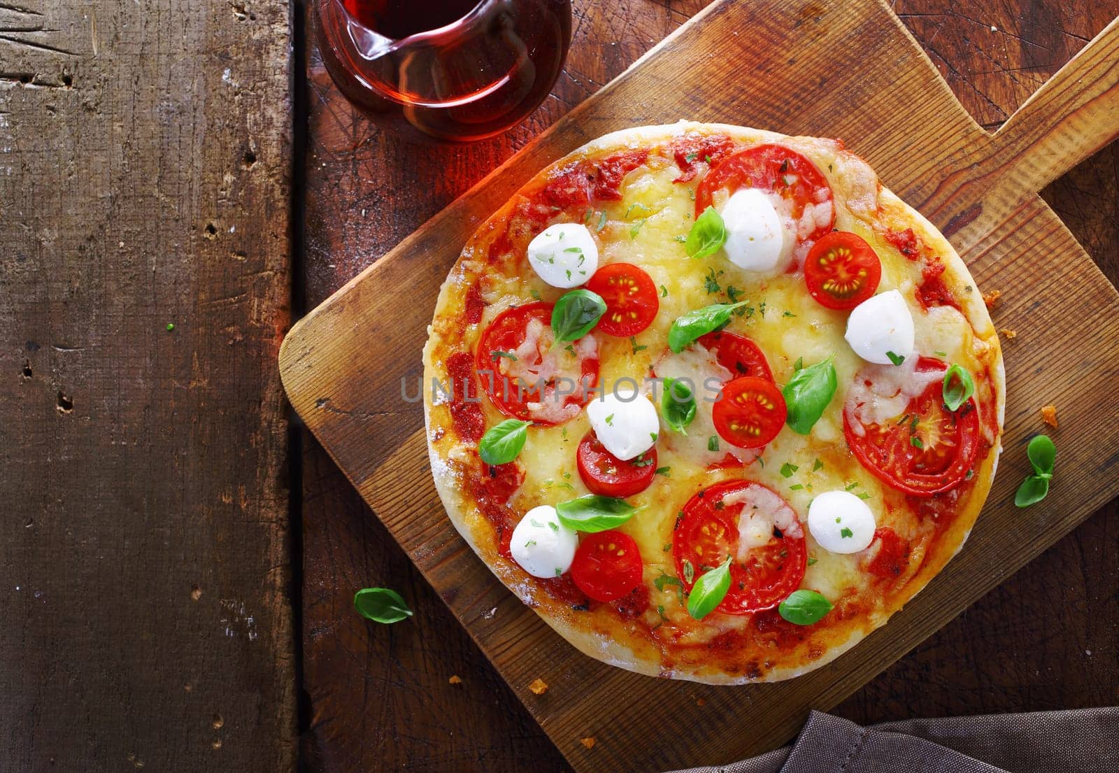 Overhead view of a colourful gourmet Italian pizza with a variety of cheeses, tomato and fresh basil on a wooden chopping board on an old rustic wooden table with copyspace