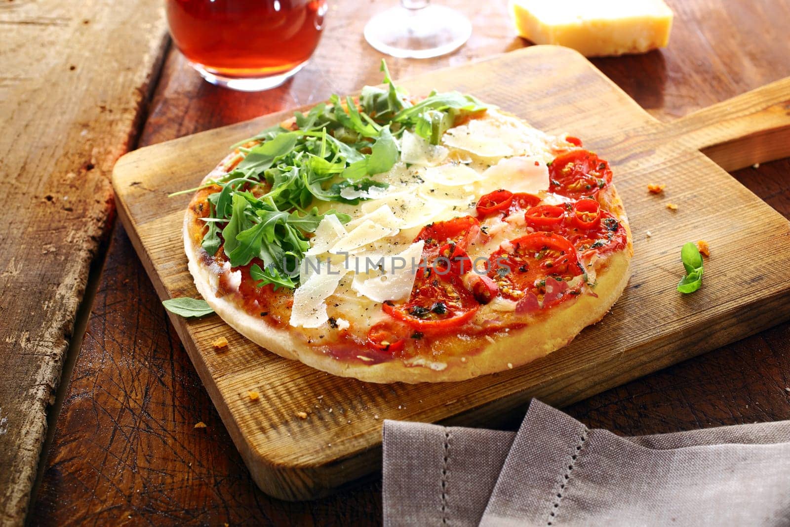 Colourful Italian pizza in the national colours topped with fresh green rocket leaves, white shavings of cheese and red tomatoes in three stripes standing on a wooden board on an old rustic table