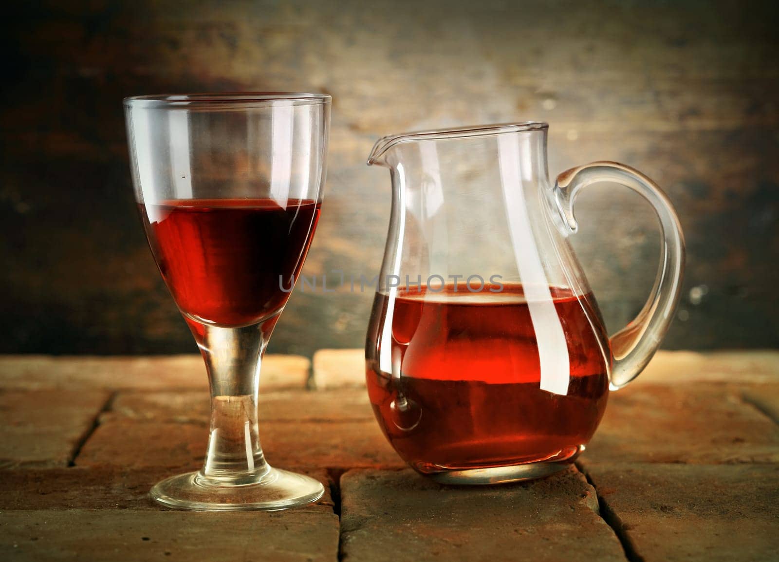 A glass of red wine with a jug of wine on a rustic table.