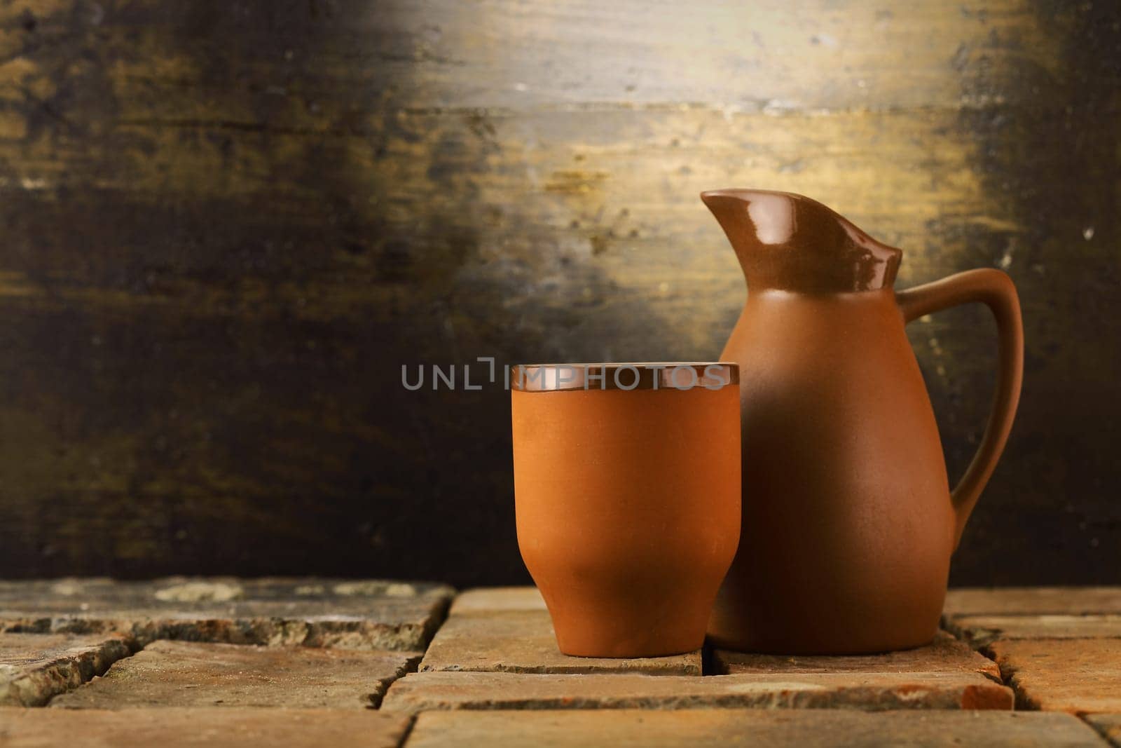 Earthenware mug and pitcher standing on grunge flagstones or tiles in a rustic cellar with copyspace