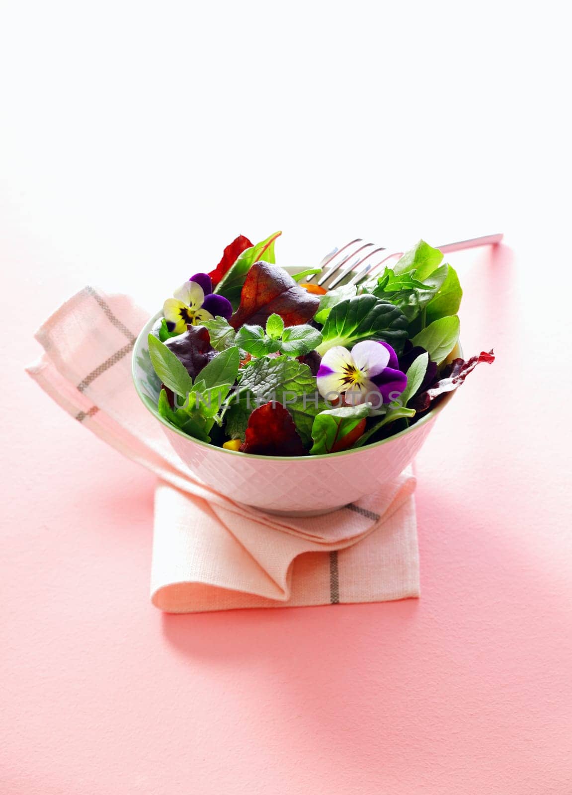 Individual serving of fresh herb salad with nasturtium flowers in a porcelain bowl served as an accompaniment to a meal on a white table napkin