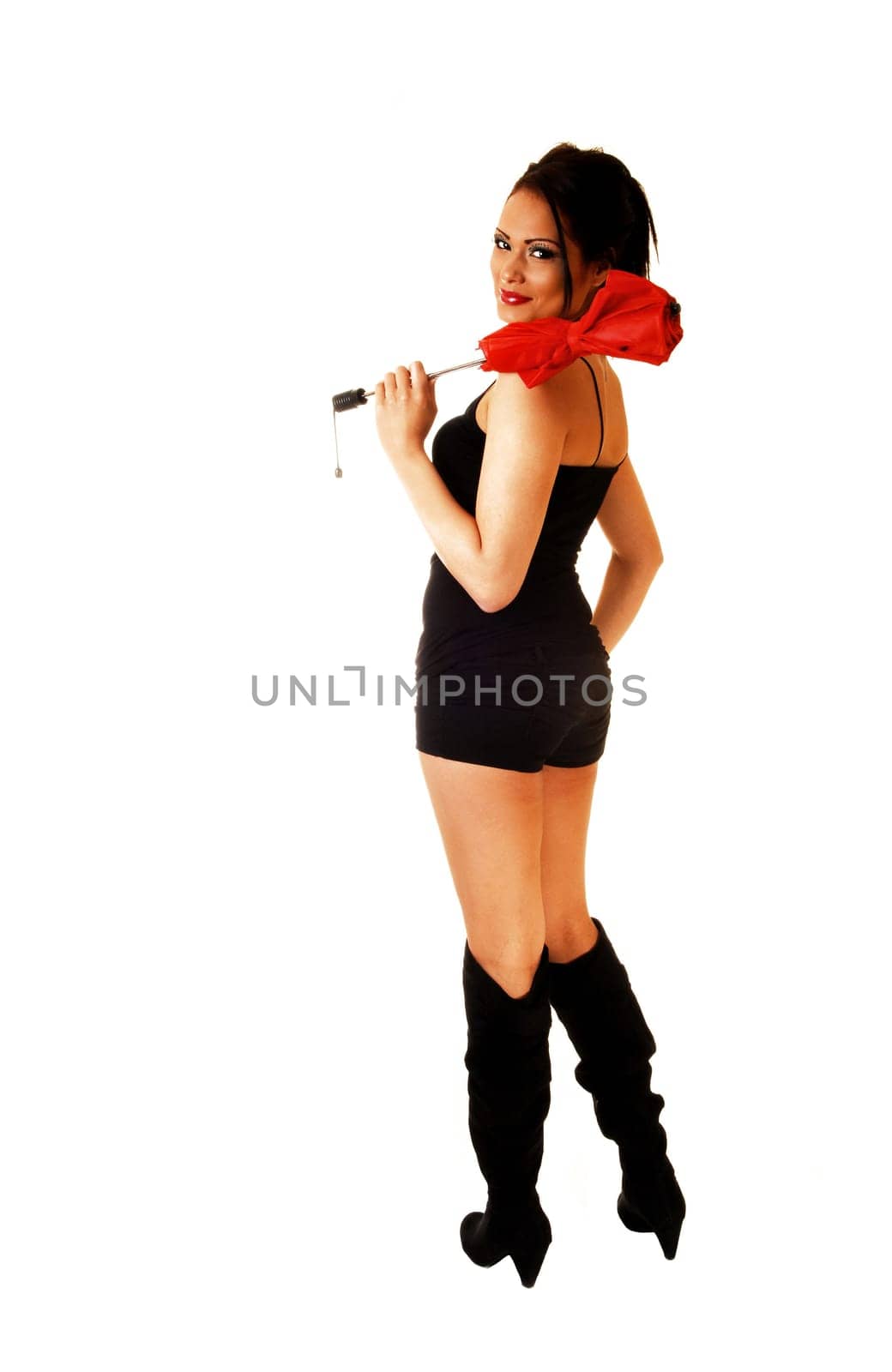 A lovely young woman standing for white background in black shorts and boots from the back, holding a red umbrella on her shoulder.