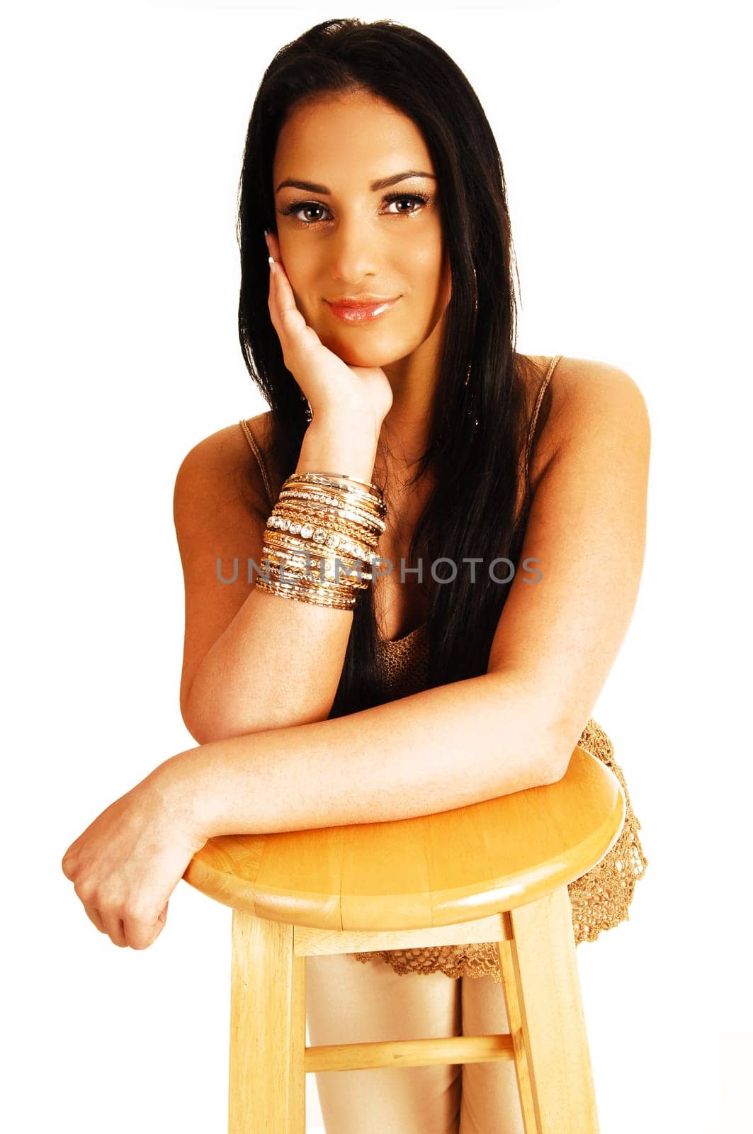 A beautiful teenager girl with her long black hair kneeling for a chair with her hands under her chin looking into the camera for white background.