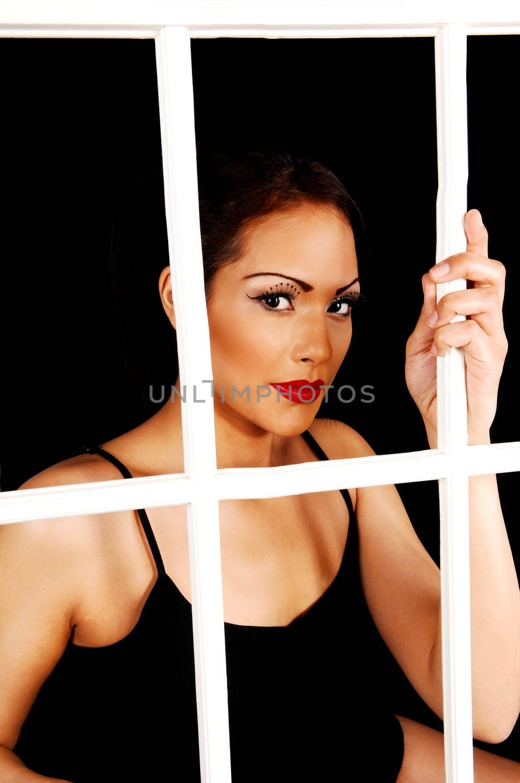 A pretty woman with nice makeup looking trough a white window frame for black background in a black t-shirt.