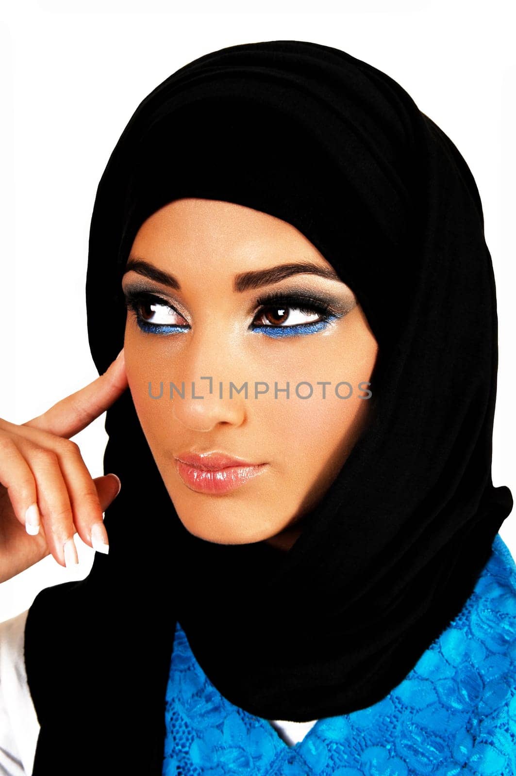 A pretty and young teen girl with a black headscarf and nice makeup looking into the camera with one finger on her face for white background.