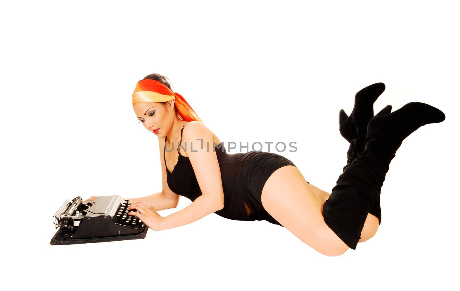 A pretty girl in black shorts and long boots lying on the floor for white background and typing on an old typewriter.