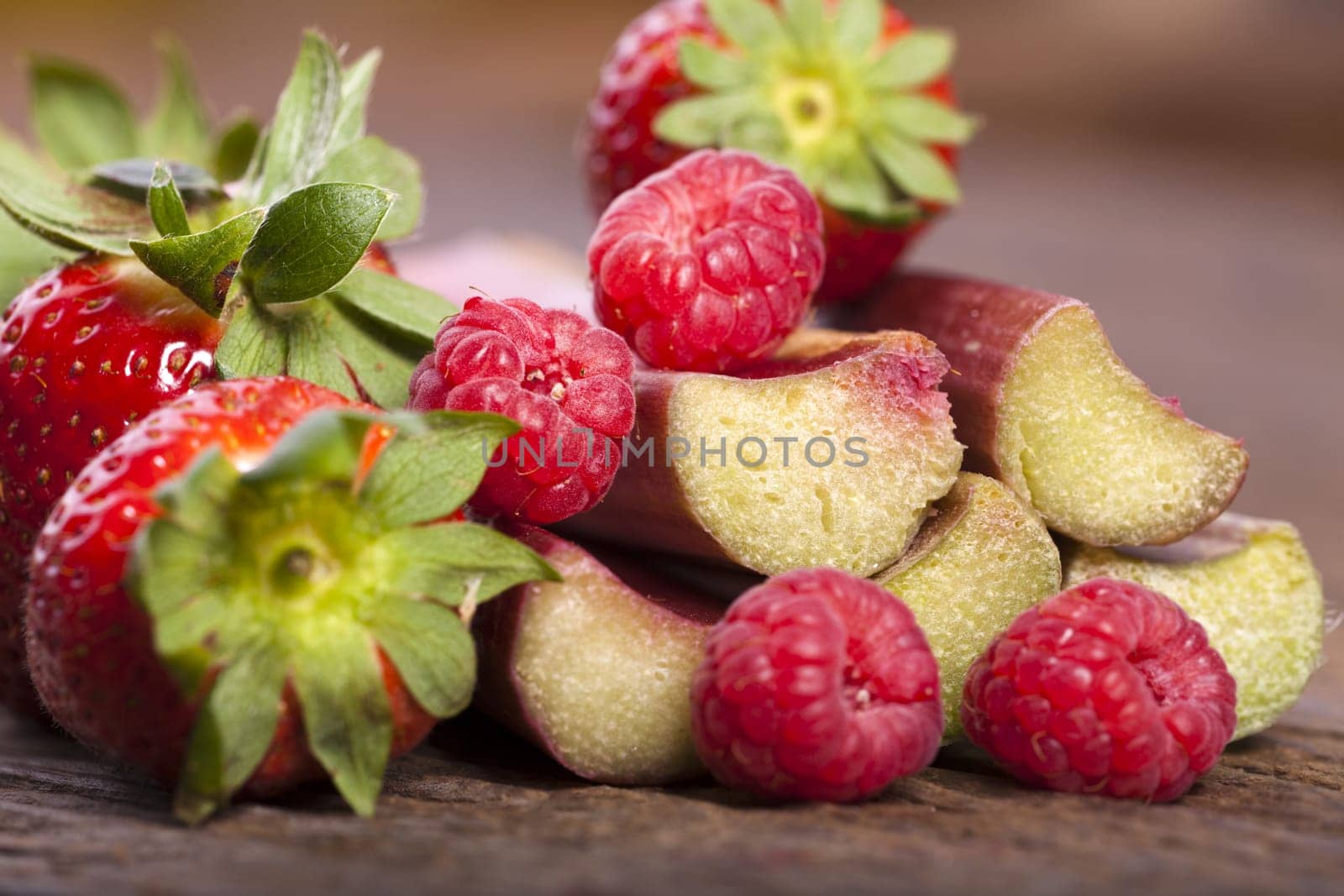 Macro shot of fresh strawberries,rhubarb sticks and raspberries on wooden background