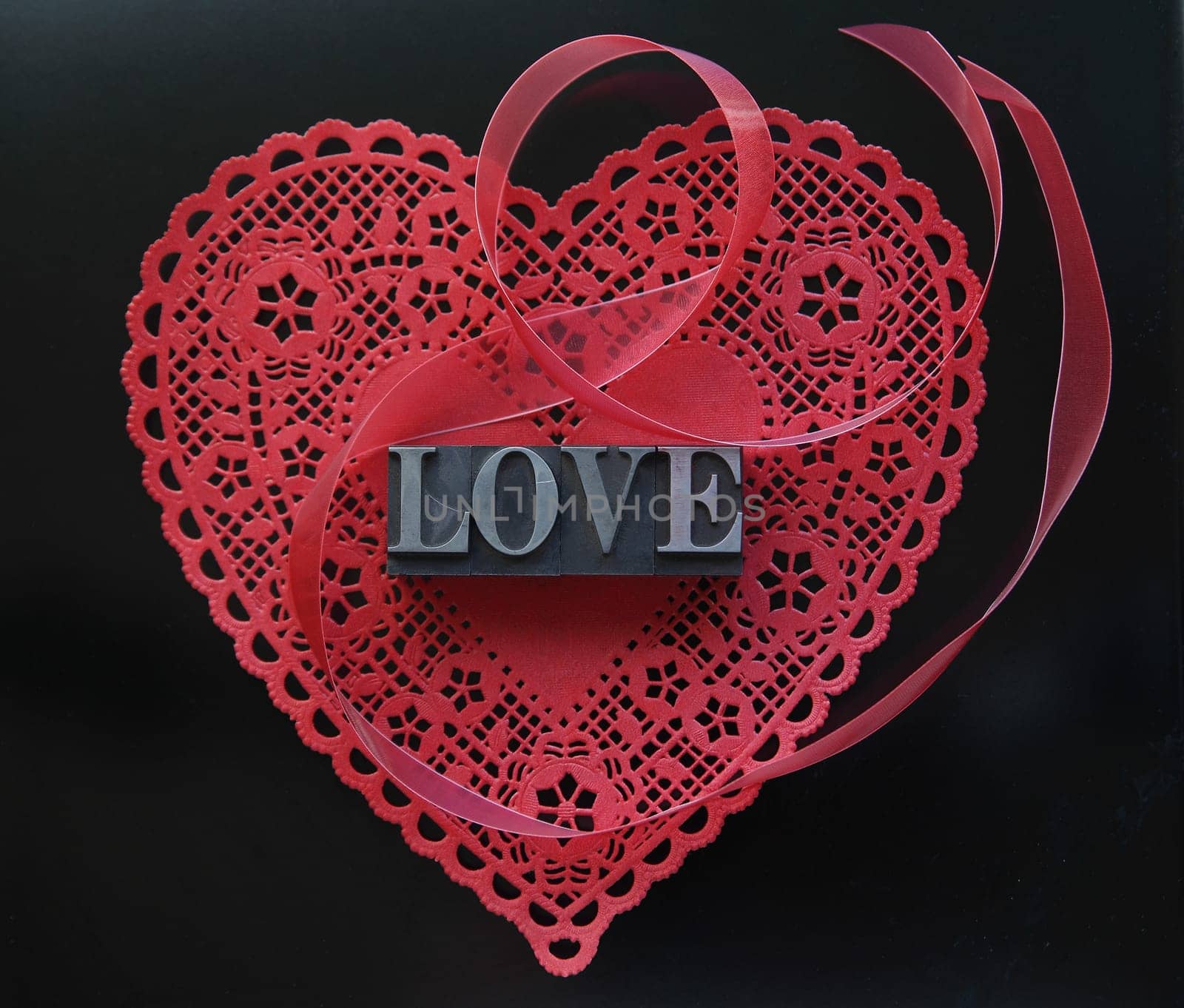 Valentine doily with the word love in metal type and a red ribbon