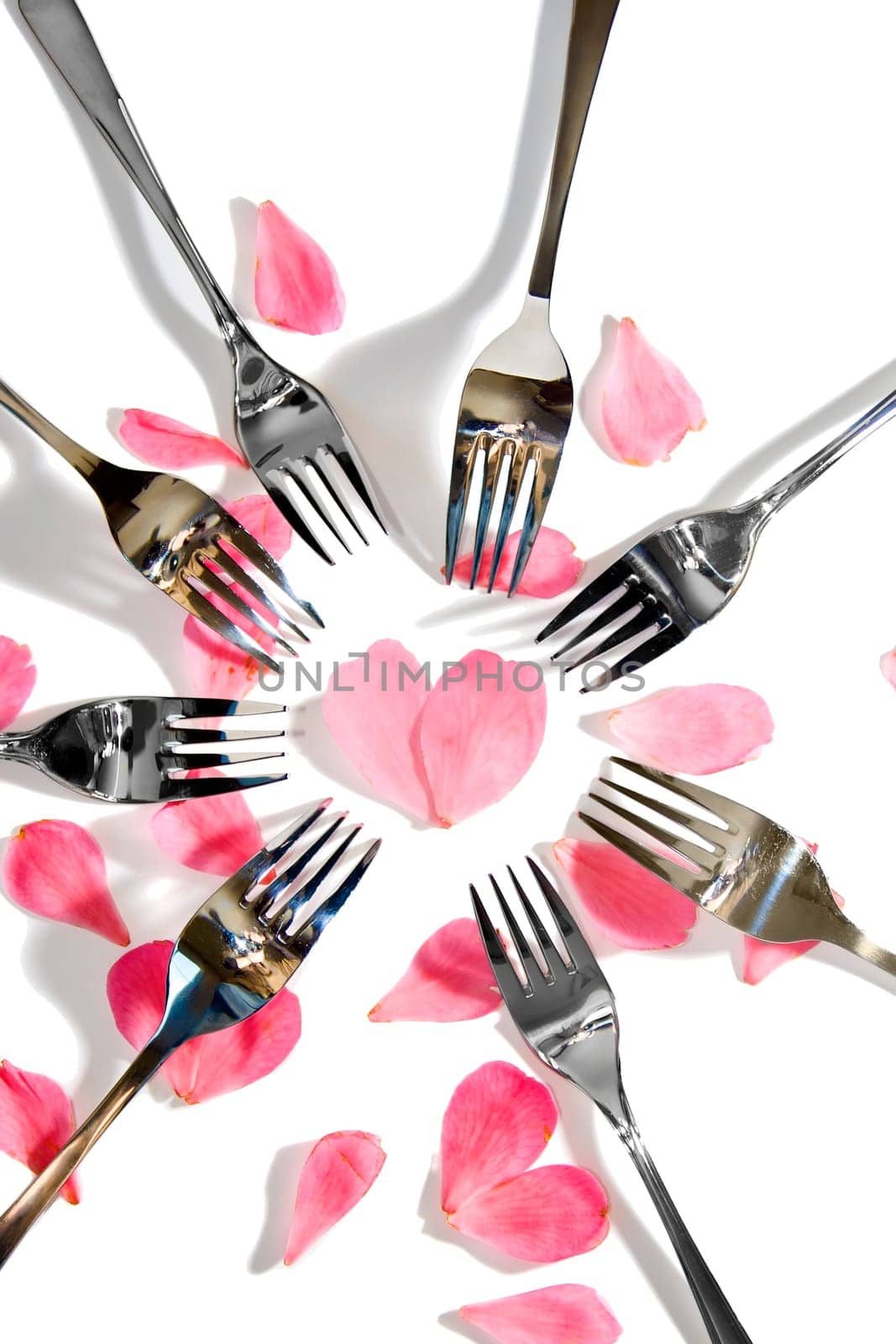 forks surrounding a heart shape petal with rose petals for a concept on romantic dining on white background