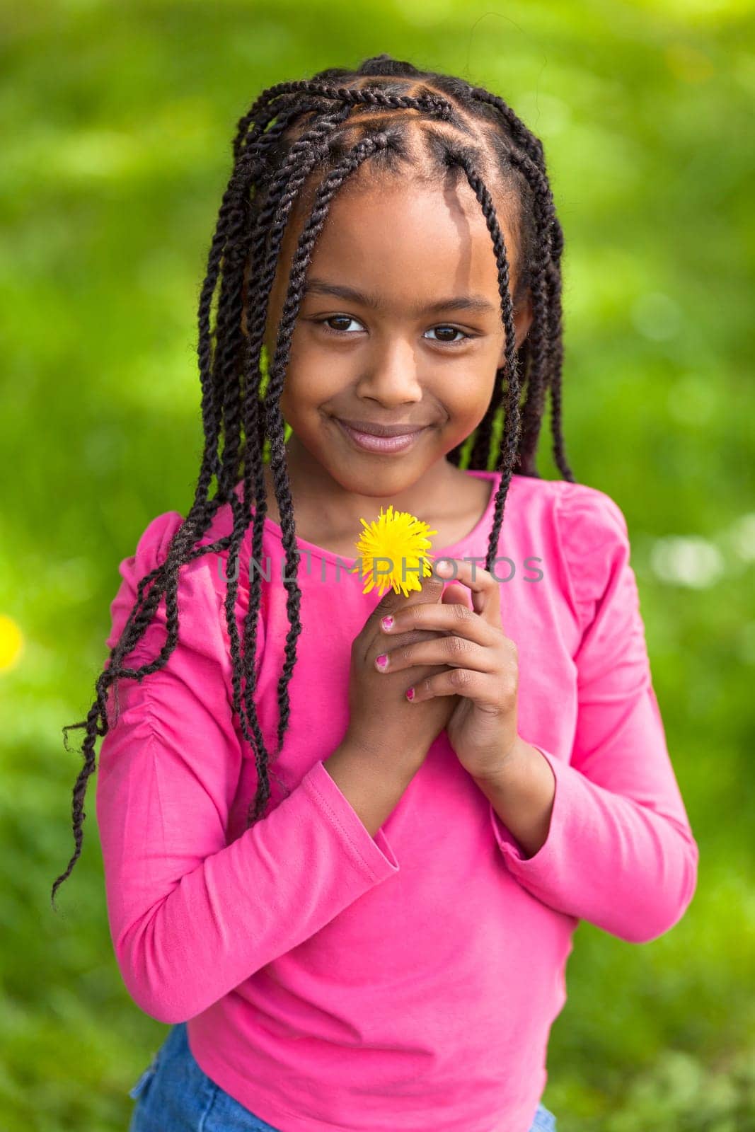 Outdoor portrait of a cute young black girl holding a dandelion flower - African people