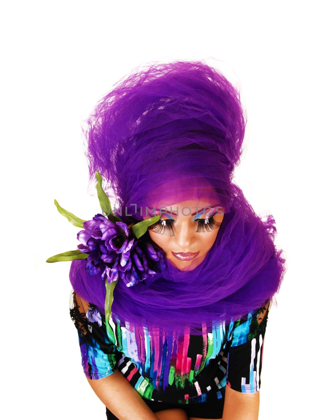 A young woman standing for white background with purple twill around her and long eye lashes, looking down.