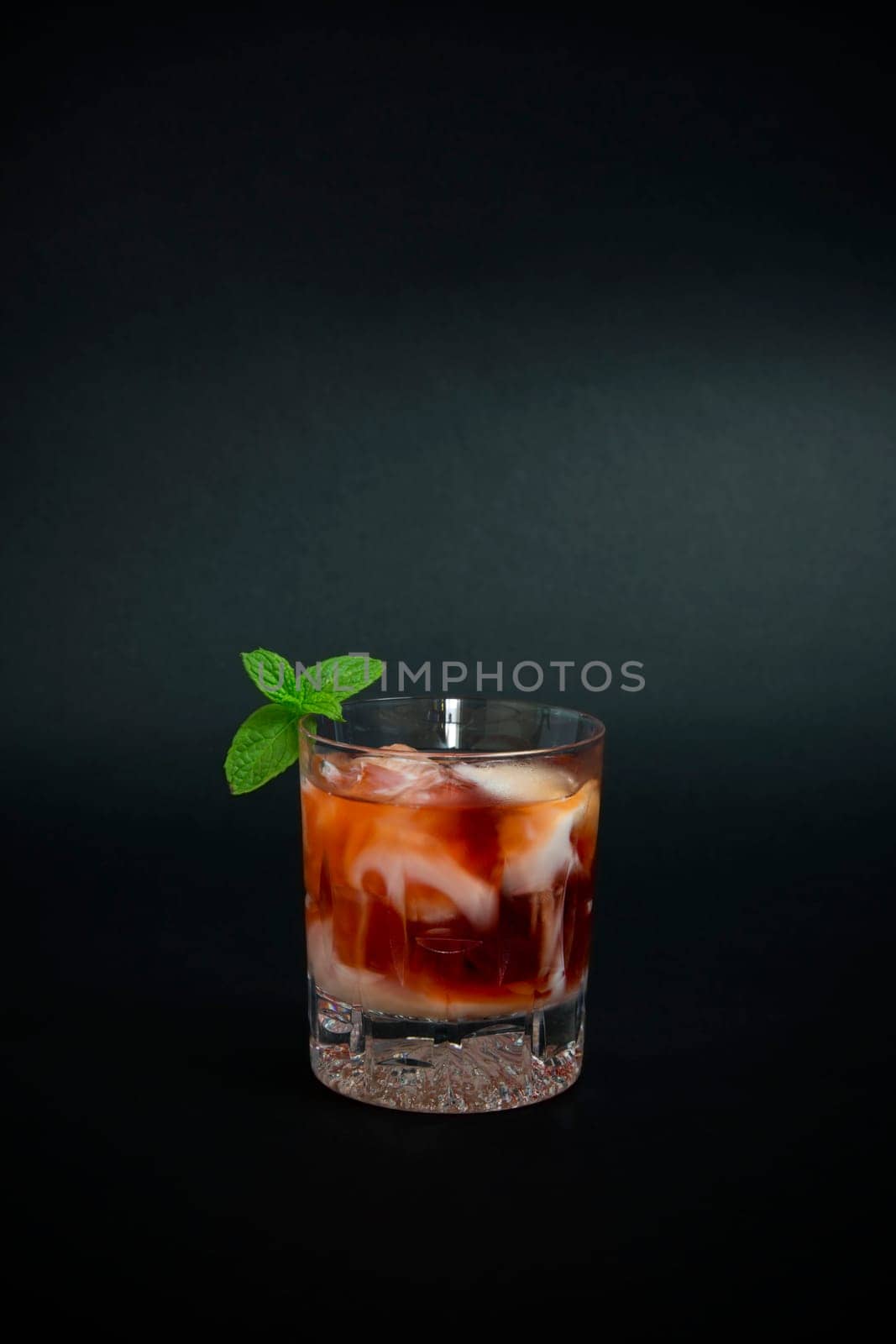 Cocktail made with red liquor, vodka and a few drops of white yogurt liquor decorated with mint leaves on dark background.