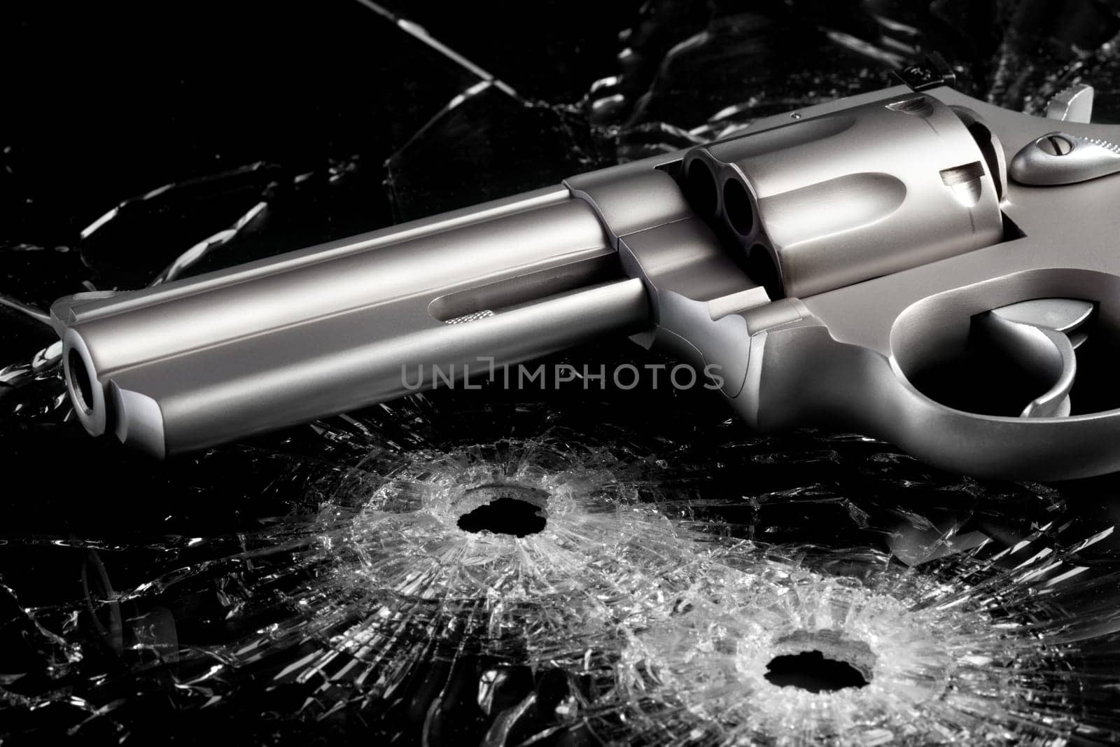 Gun with two bullet holes in glass over black - modern revolver close up