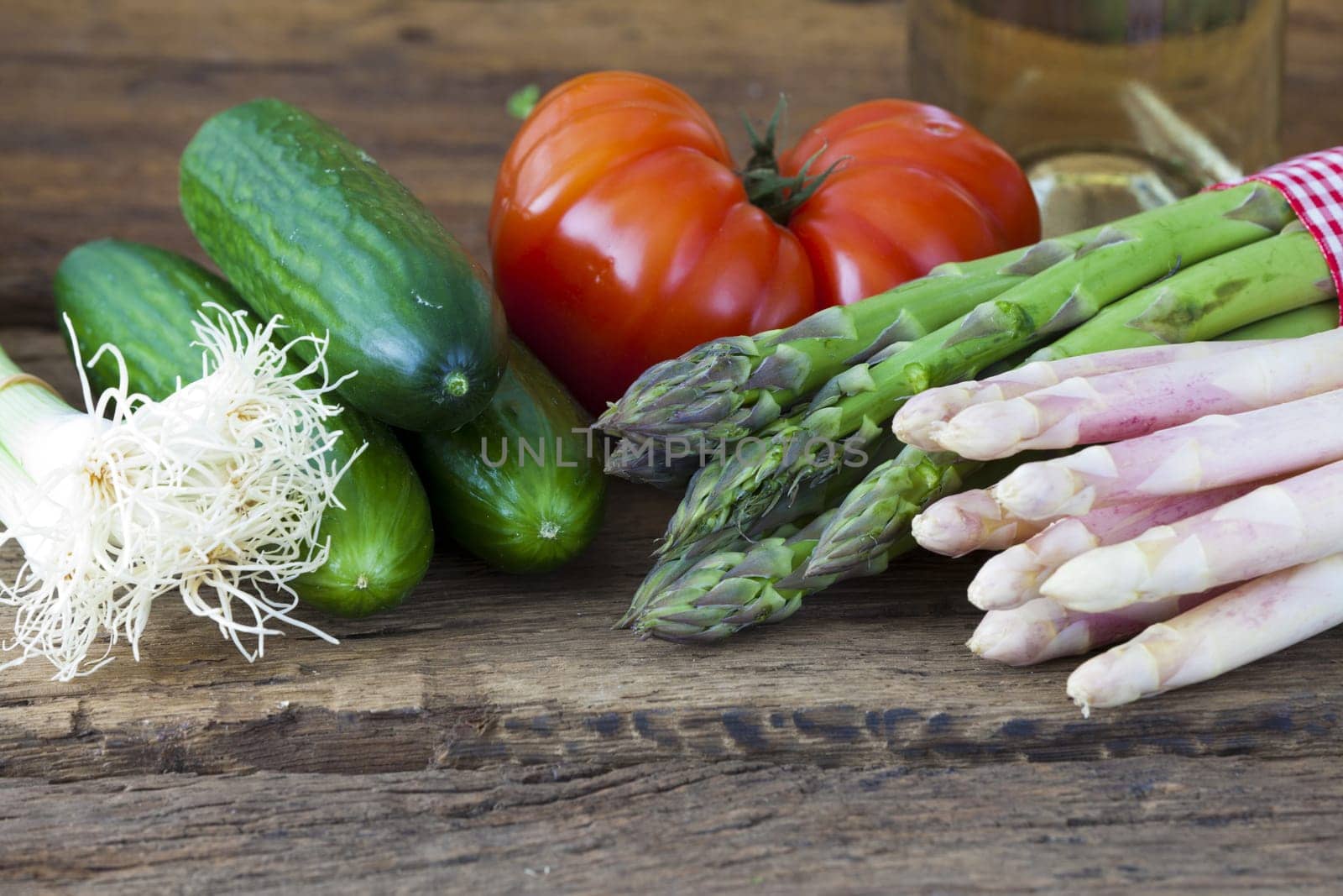 Green and white asparagus with beef tomato,spring onions and cucumbers on a rustic wooden surface