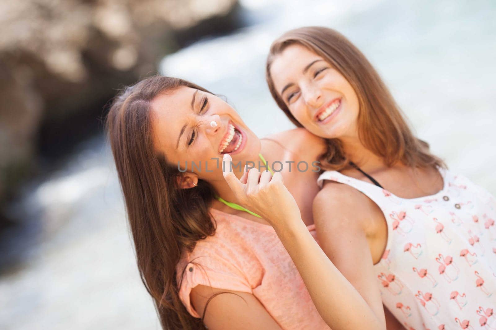 Happy young woman applying cream on girlfriend's nose
