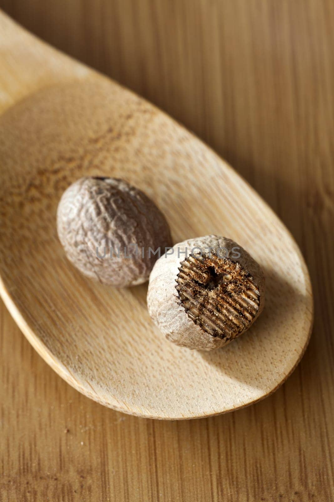 Two nutmegs on a wooden spoon on a wooden surface