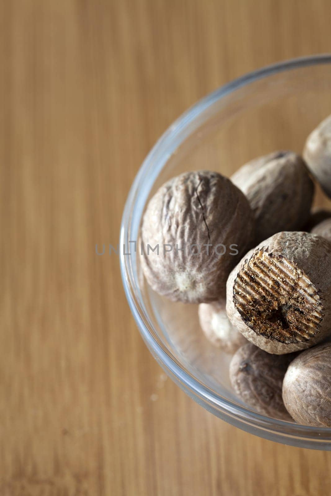View from above to a glass bowl with some whole and a rubbed nutmeg