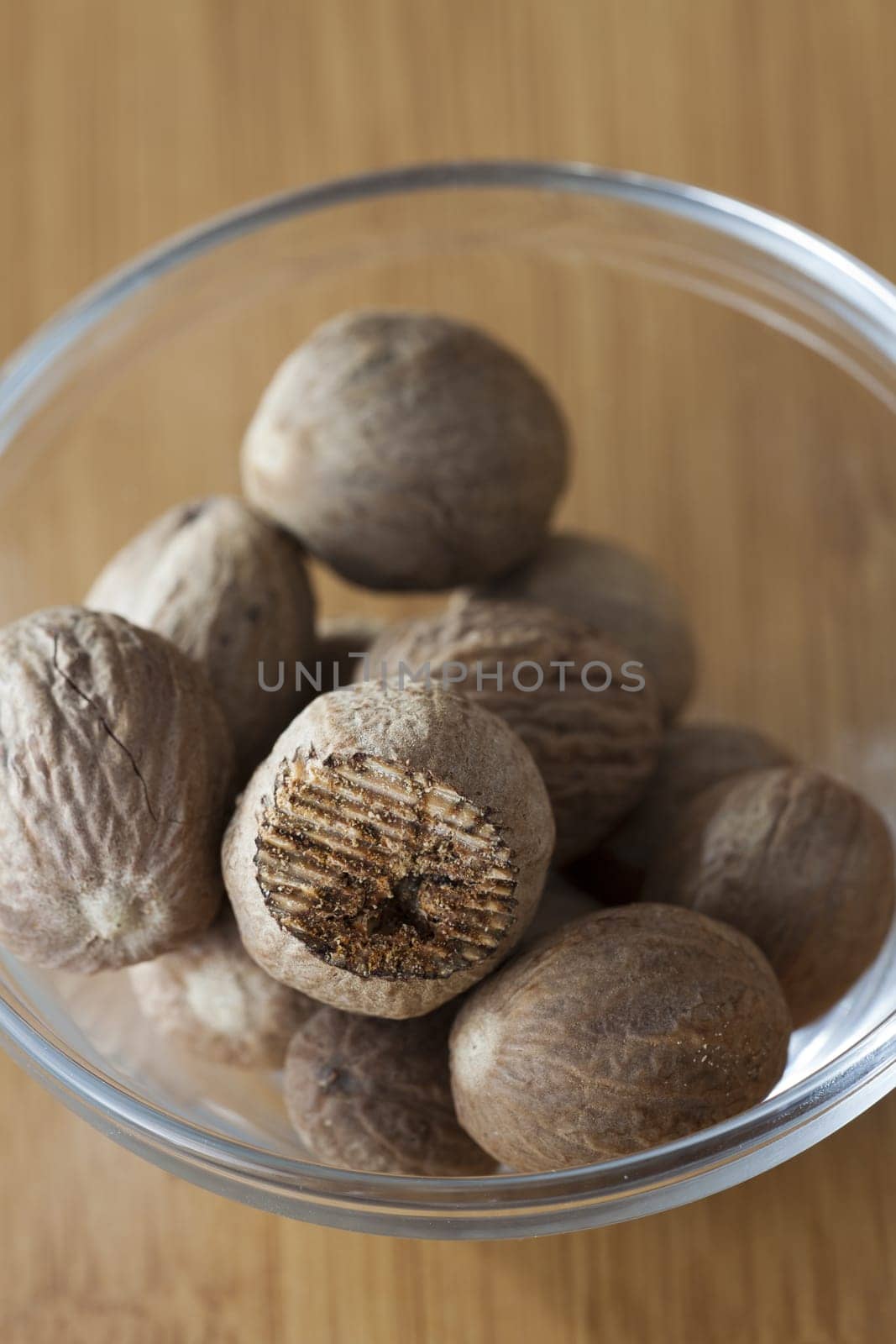 View from above to a glass bowl with some whole and a rubbed nutmeg