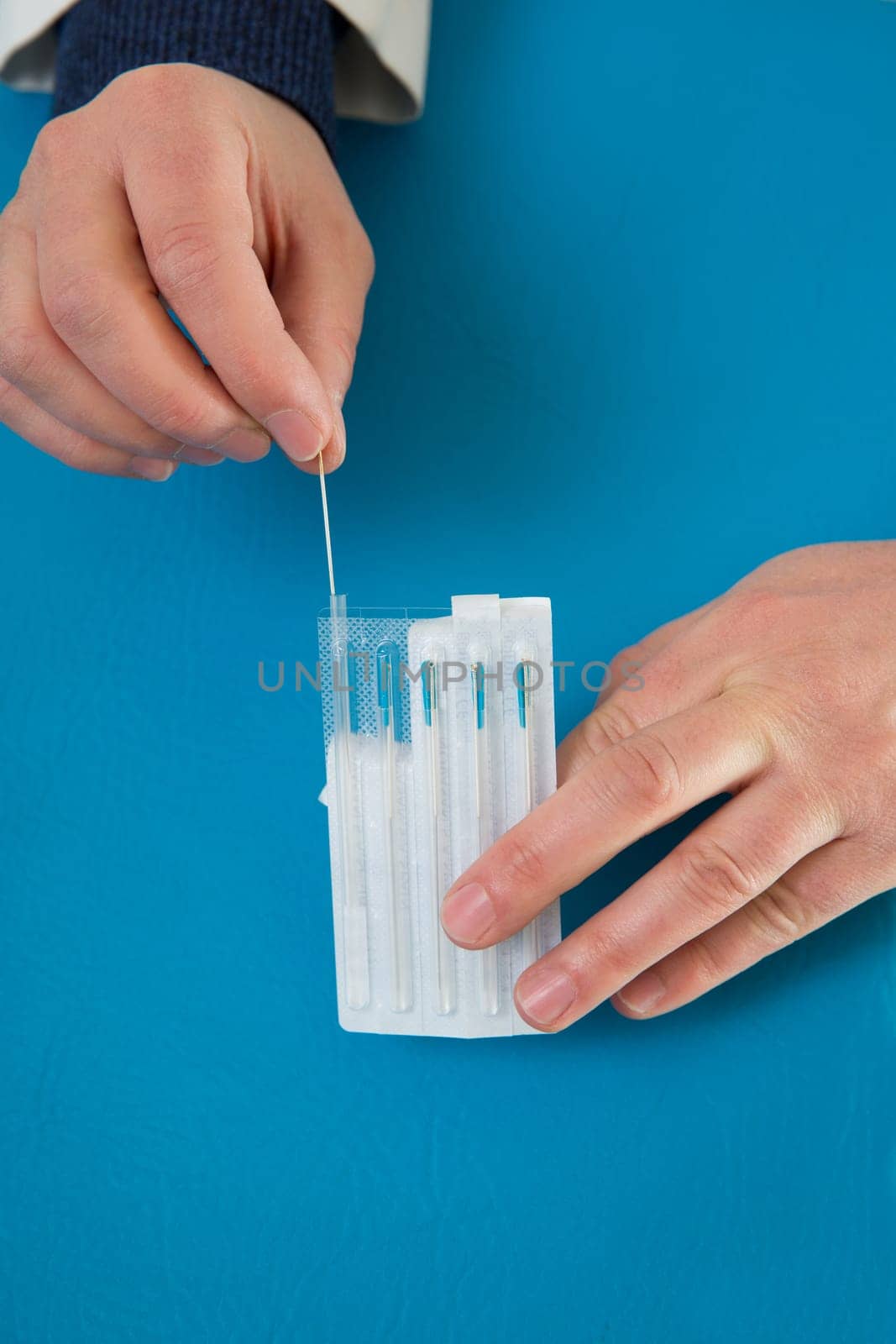 Acupuncture needles in doctor hands holding blister on blue
