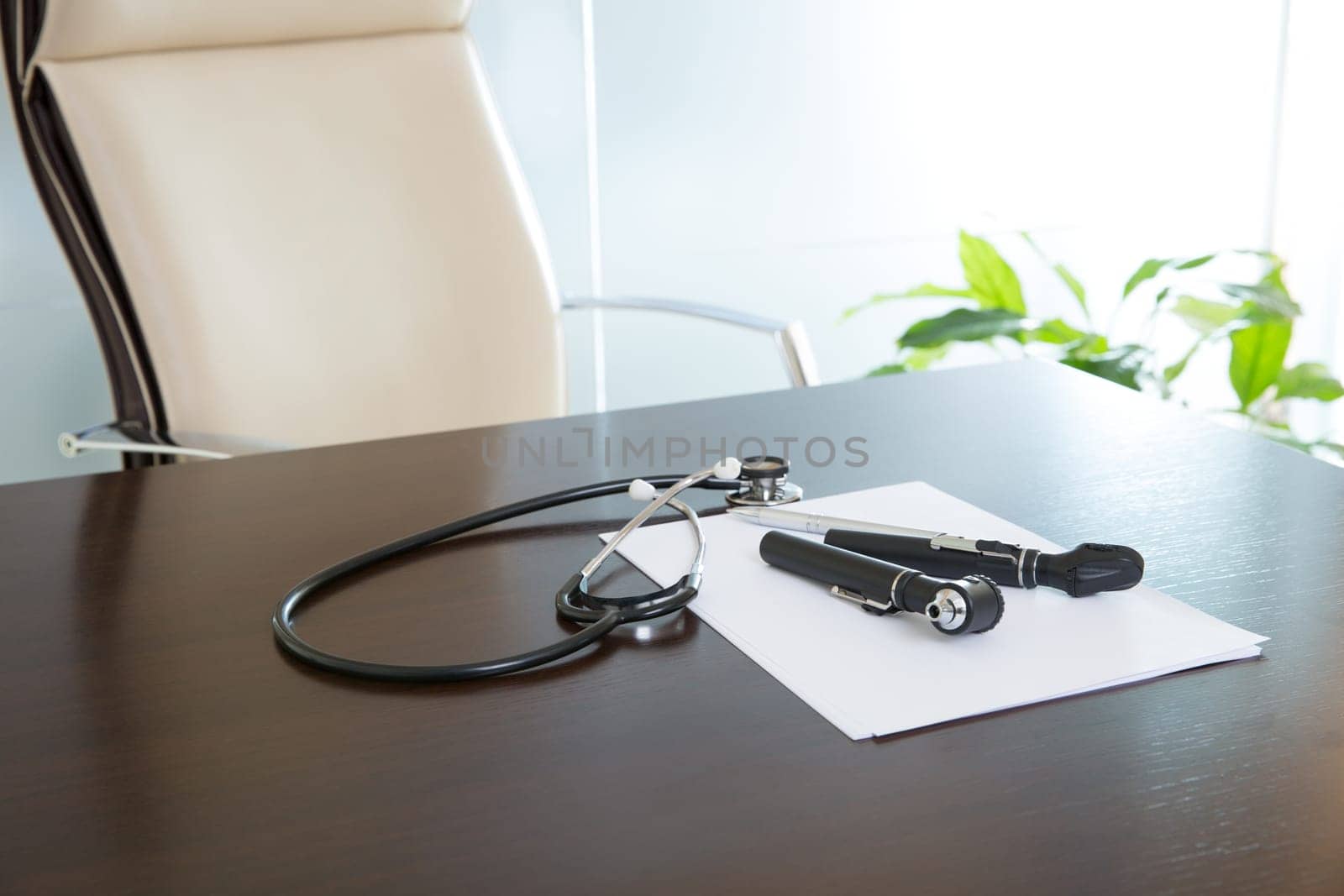 Doctor office table desk and beige chair with stethoscope otoscope and white paper