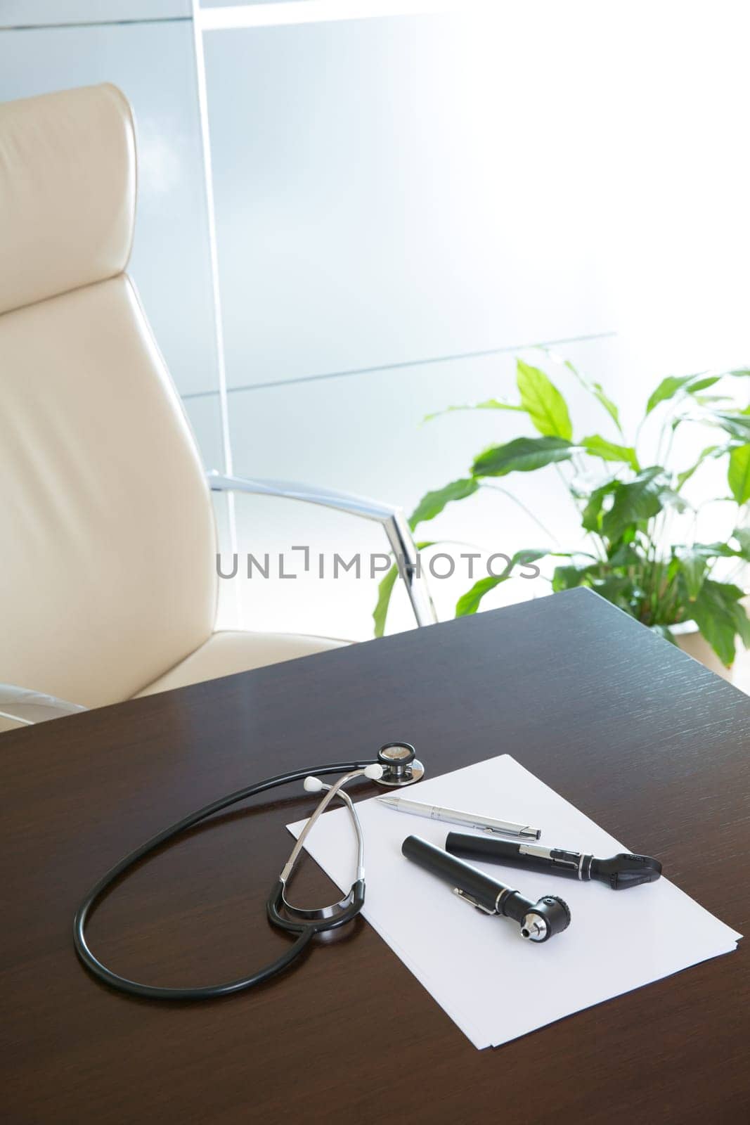 Doctor office table desk and beige chair with stethoscope otoscope and white paper