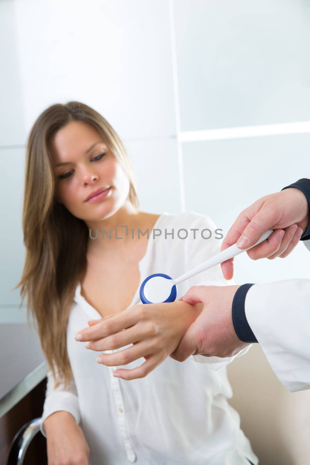 Doctor checking wrist with reflex round hammer to woman patient in hospital