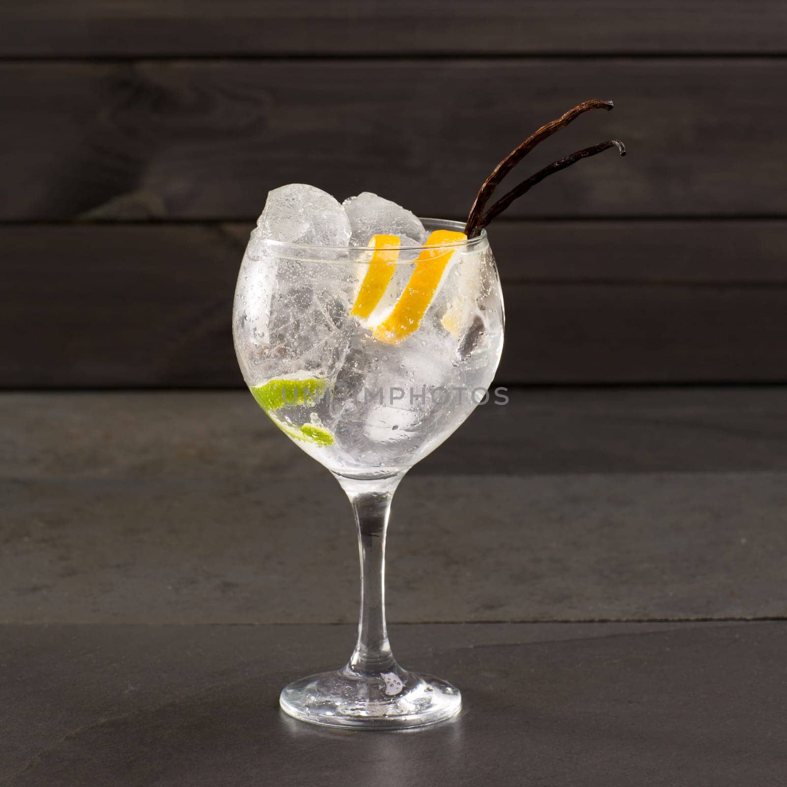 Gin tonic cocktail with ice vanilla lima and lemon on black background