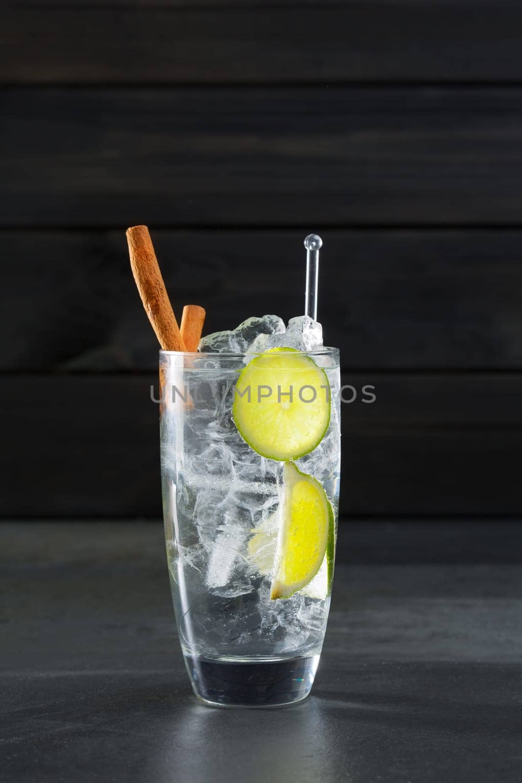 Gin tonic cocktail with lima cinnamon and ice cube on black background